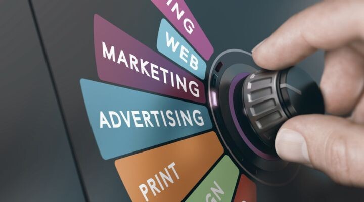 Una mano gira un dial que presenta secciones etiquetadas: Estrategia de comunicación, Web, Marketing, Publicidad, Impresión, Diseño.