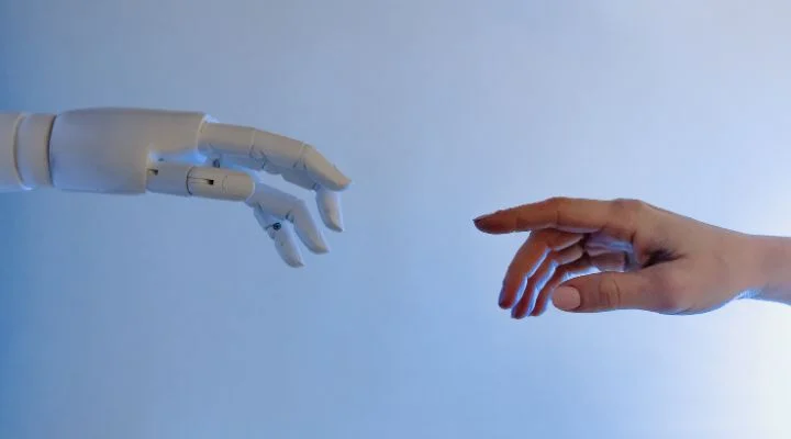 Una mano robótica y una mano humana, que representan el impacto revolucionario de Gen IA, se extienden una hacia la otra sobre un fondo azul.