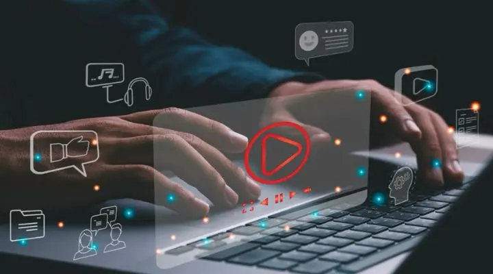 Manos escribiendo en una computadora portátil con íconos digitales flotantes que representan medios, funciones de comunicación y publicidad.