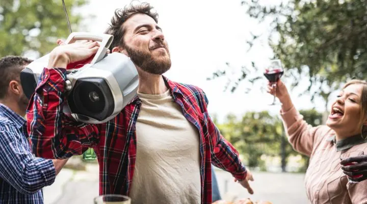 Un hombre lleva un equipo de música sobre su hombro, recordando la época de la radio, mientras la gente a su alrededor aplaude con copas de vino tinto.