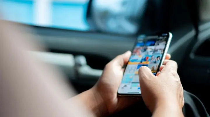 En medio del bullicio, una persona sostiene un teléfono inteligente con ambas manos, navegando por una galería de fotos.