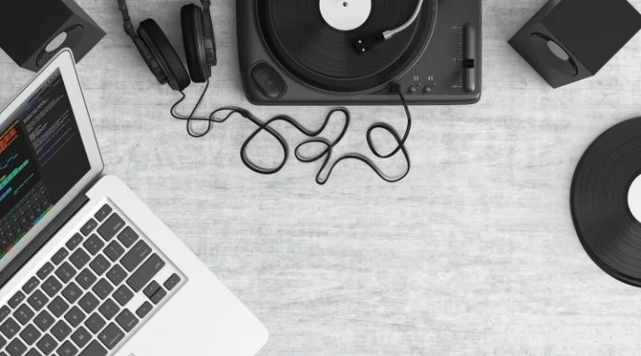 Sobre una superficie gris claro se encuentra la esencia de cualquier proceso creativo: una computadora portátil, unos auriculares, un tocadiscos que hace girar vinilos y unos elegantes altavoces.