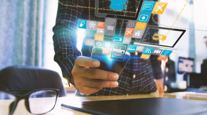 Una persona sostiene un teléfono inteligente con varios íconos de aplicaciones, resaltando la facilidad de seleccionar medios, mientras flotan sobre él junto a anteojos y documentos en un escritorio.