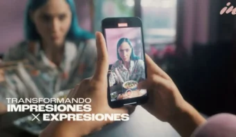 Una persona de cabello azul está sentada, sosteniendo palillos y siendo fotografiada con un teléfono inteligente. El texto superpuesto dice: "TRANSFORMANDO IMPRESIONES X EXPRESIONES".