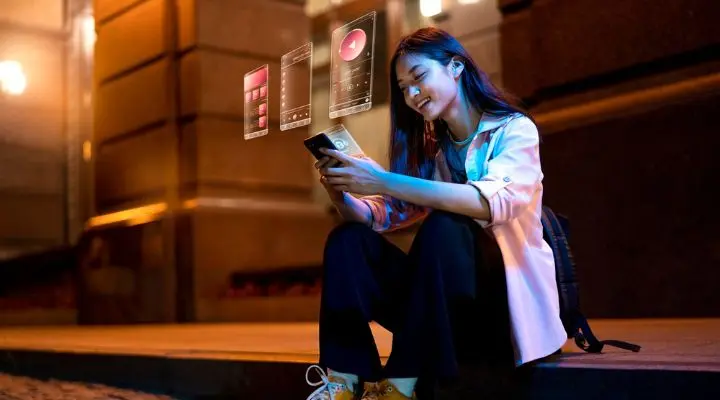 Una persona está sentada al aire libre por la noche, sonriendo mientras usa su teléfono inteligente en medio de la saturación de información. Íconos digitales flotantes muestran música e interfaces de aplicaciones frente a ella.