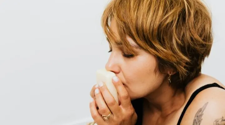 Persona de cabello corto sostiene un objeto de color claro cerca de su cara, con los ojos cerrados, de manera contemplativa, como si reflexionara sobre la esencia del marketing de los aromas.
