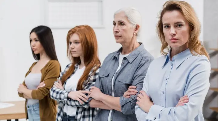 Cuatro mujeres de diferentes edades permanecen en el interior con los brazos cruzados, encarnando la esencia de lo femenino mientras miran hacia adelante con confianza.
