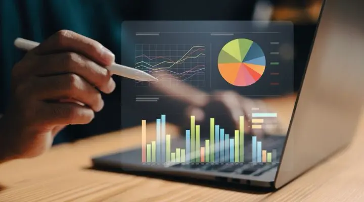 Una persona usa un lápiz óptico mientras visualiza gráficos y tablas digitales en una computadora portátil, incluido un gráfico circular y gráficos de barras que representan el análisis de datos para campañas de compra de medios.