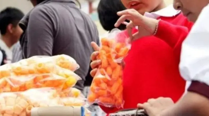 Personas sosteniendo y vendiendo bolsas de comida en un mercado al aire libre, donde la atmósfera vibrante está salpicada de los tentadores aromas de la comida chatarra.