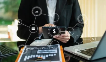 Una persona vestida de negocios usa una tableta en un escritorio con una computadora portátil y documentos; se superponen íconos digitales relacionados con las finanzas, incluidos los que hacen referencia a la Comisión de Defensa, que representan la tecnología financiera y el análisis de datos.