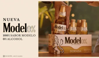 Una mano extrae una botella de Model0% Dorada de un pack de seis. El envase indica que no contiene alcohol: «100% sabor Modelo, 0% alcohol».