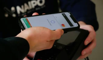Una persona sostiene un teléfono inteligente cerca de una terminal de pago para realizar un pago sin contacto utilizando una aplicación de billetera digital, mostrando la conveniencia que ofrecen los neobancos en México.