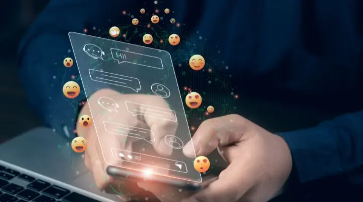 Una persona escribe en un teléfono inteligente con burbujas de chat digitales, emojis y  los "likes" que aparecen sobre la pantalla, simbolizando la mensajería y la comunicación en línea.